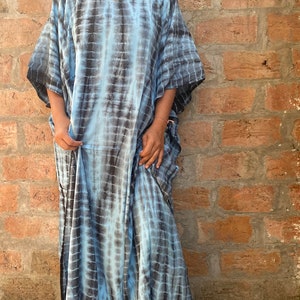 May include: A long, flowing blue and black tie-dye kaftan with a V-neckline and short sleeves. The kaftan is made of a soft, comfortable fabric and has a relaxed fit.