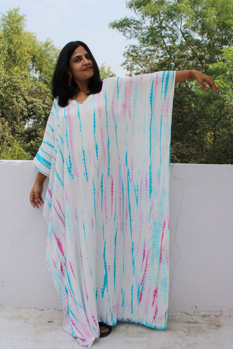 May include: A white maxi dress with a tie-dye pattern in shades of pink and blue. The dress has a loose, flowing fit and a V-neckline.
