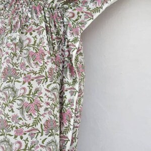 May include: A white kaftan with a pink and green floral print. The kaftan has a drawstring waist and a V-neck.