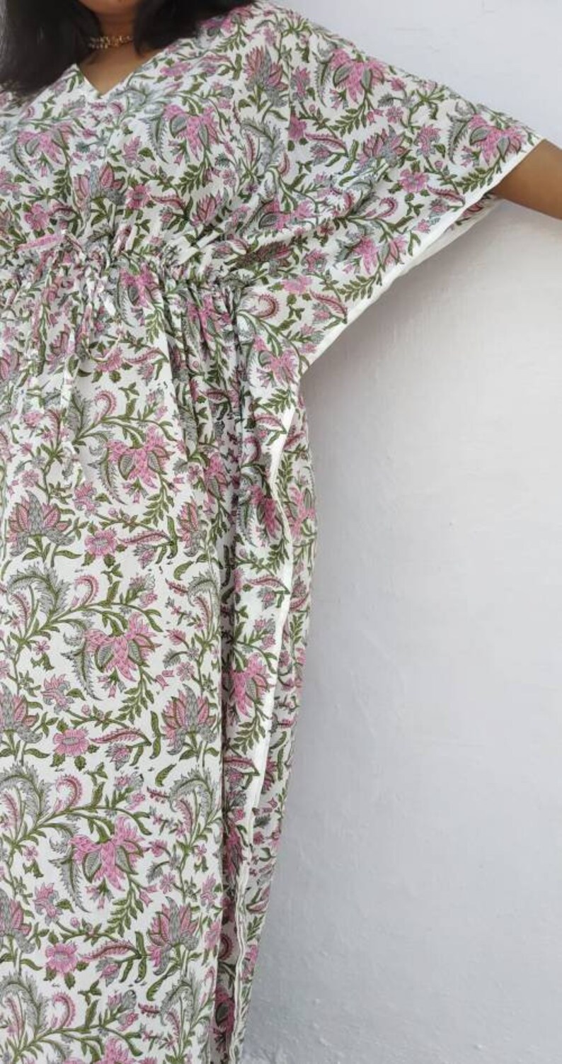 May include: A white kaftan with a pink and green floral print. The kaftan has a drawstring waist and a V-neck.