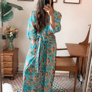 May include: A woman wearing a long, blue and orange floral print robe with a tie belt. The robe has a relaxed fit and is made of a lightweight fabric.