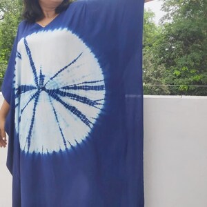 Op de afbeelding: Een blauwe en witte tie-dye maxi-jurk met een rond patroon. De jurk heeft een V-hals en lange mouwen.