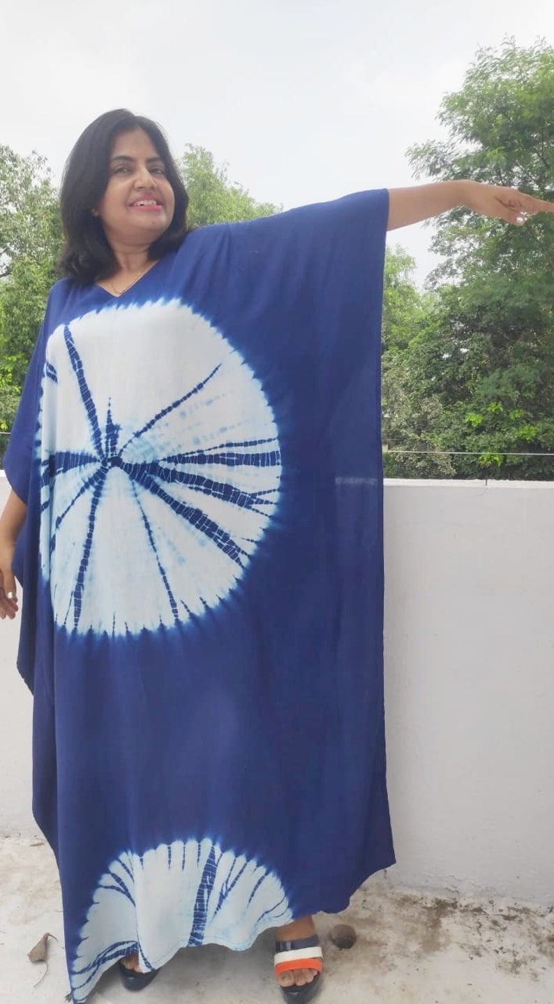 Op de afbeelding: Een blauwe en witte tie-dye maxi-jurk met een rond patroon. De jurk heeft een V-hals en lange mouwen.