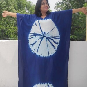 Op de afbeelding: Een lange, blauwe tie-dye kaftan met witte cirkels. De kaftan heeft een V-hals en lange mouwen.