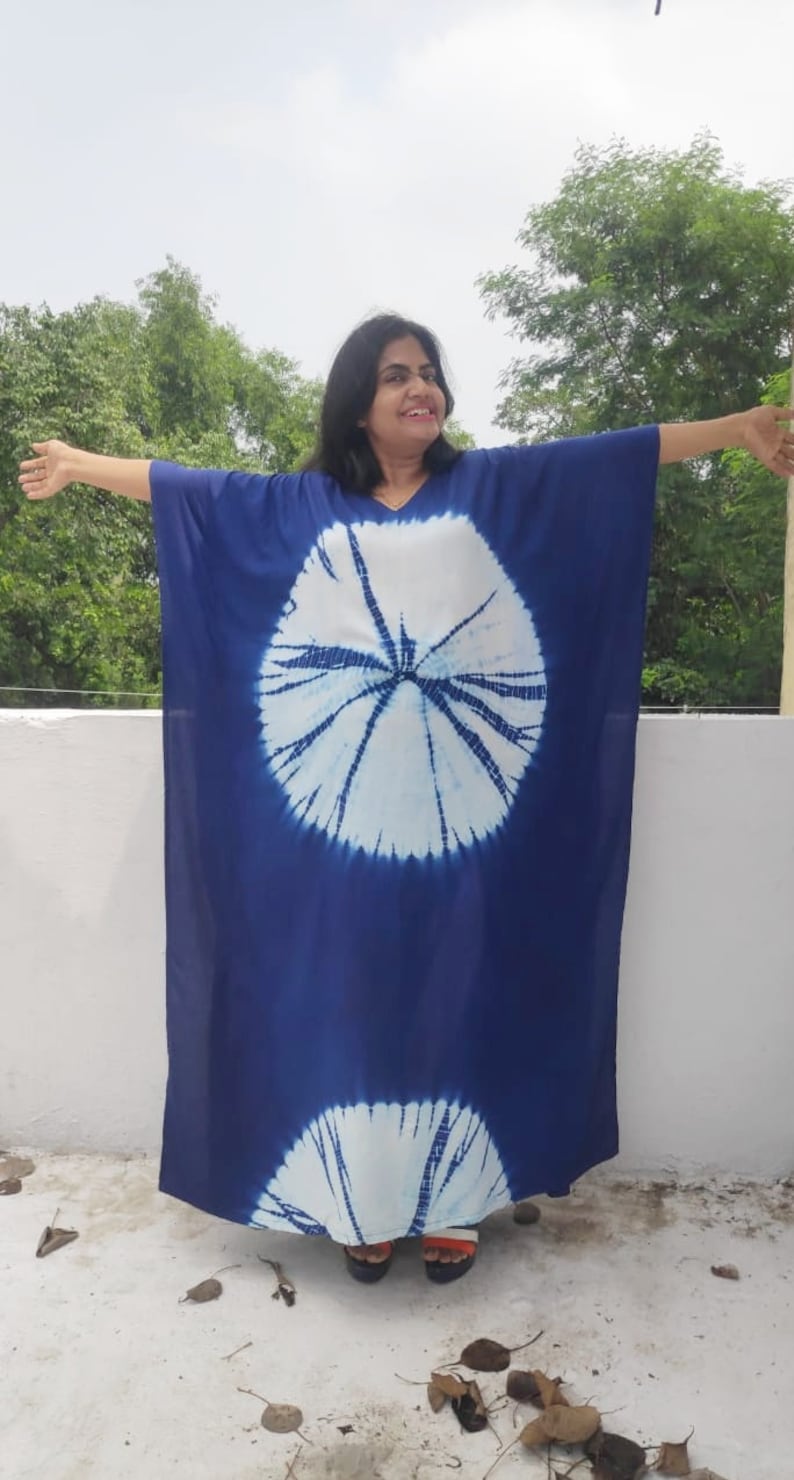 Op de afbeelding: Een lange, blauwe tie-dye kaftan met witte cirkels. De kaftan heeft een V-hals en lange mouwen.