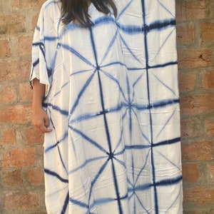 May include: A white, loose-fitting caftan dress featuring a blue geometric tie-dye design. The dress has wide sleeves and a relaxed silhouette. The fabric looks lightweight, ideal for warmer climates.