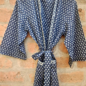 May include: A blue cotton robe with a white floral pattern and a white trim. The robe has a tie belt and a pocket on the left side.