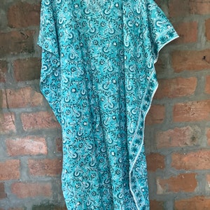 May include: A turquoise blue kaftan with a white floral pattern. The kaftan has a V-neck and short sleeves.