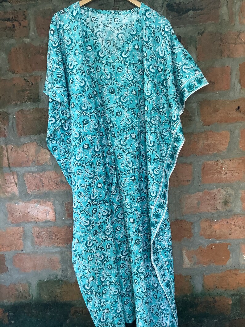 May include: A turquoise blue kaftan with a white floral pattern. The kaftan has a V-neck and short sleeves.