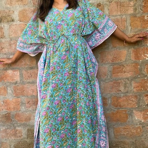 May include: A long, flowing blue and pink floral print kaftan with a drawstring waist and side slits. The kaftan is made of cotton and has a relaxed fit.