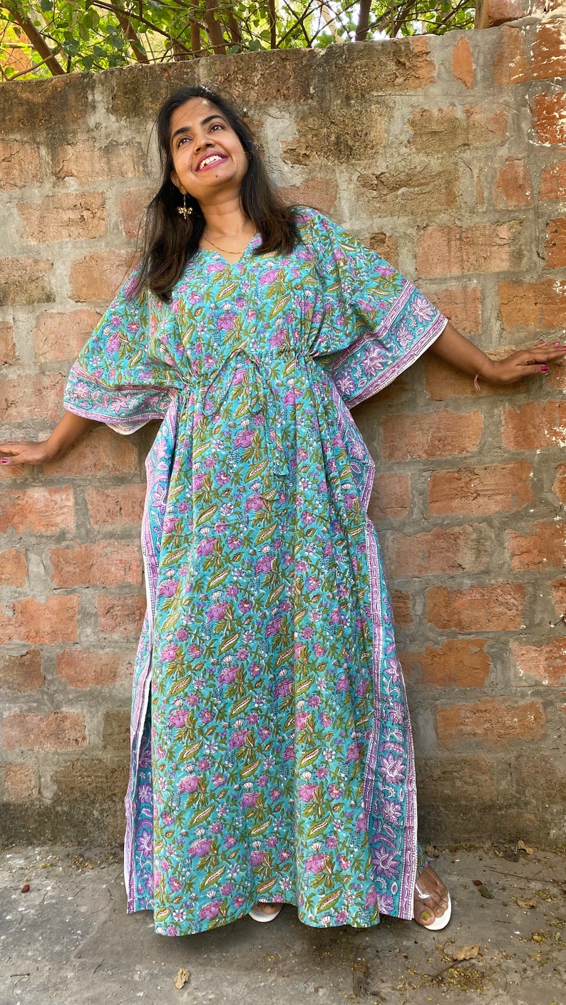 May include: A long, flowing blue and pink floral print kaftan with a drawstring waist and side slits. The kaftan is made of cotton and has a relaxed fit.