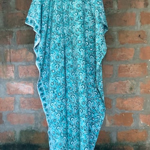 May include: A teal blue kaftan with a white floral pattern. The kaftan has a loose fit and a V-neckline.