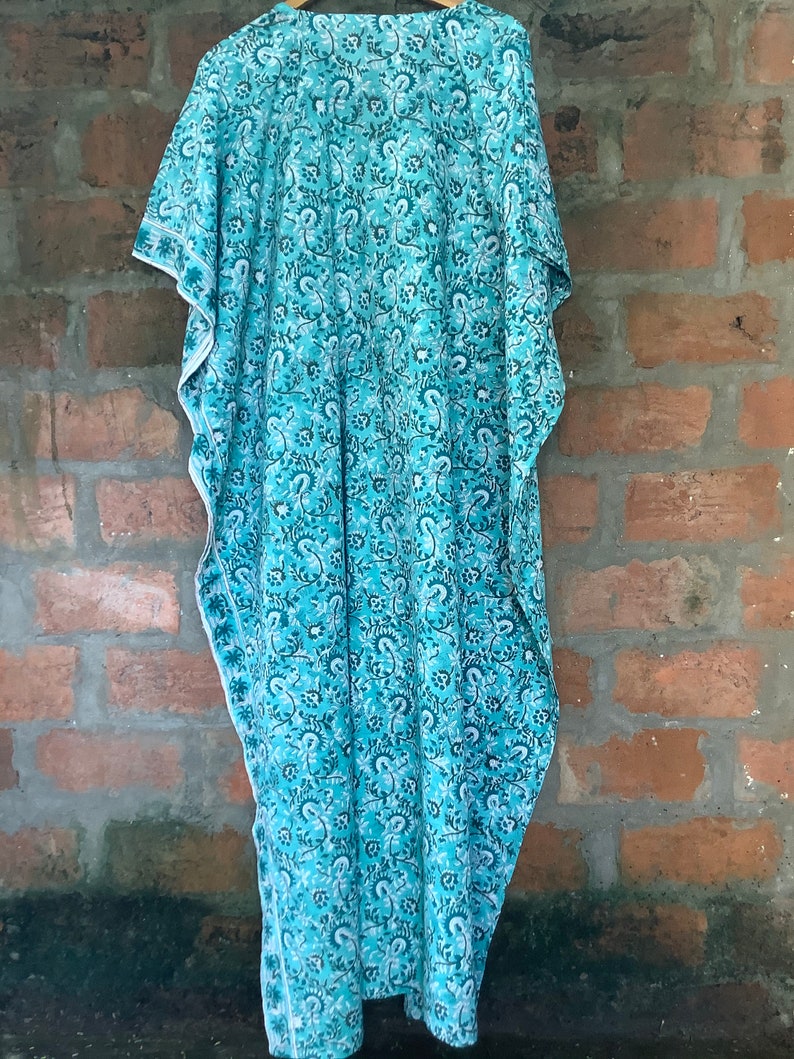 May include: A teal blue kaftan with a white floral pattern. The kaftan has a loose fit and a V-neckline.