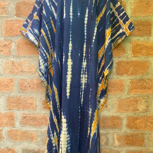 May include: A long, navy blue kaftan with a tie-dye pattern in shades of yellow and white. The kaftan has a V-neck and short sleeves.