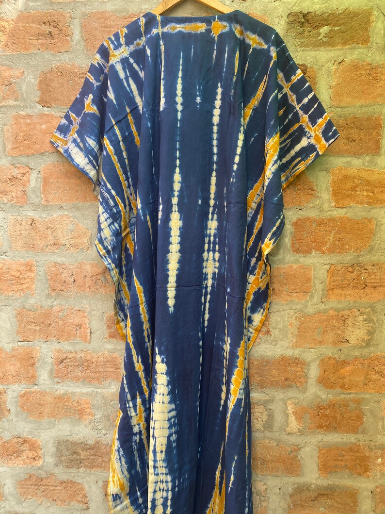 May include: A long, navy blue kaftan with a tie-dye pattern in shades of yellow and white. The kaftan has a V-neck and short sleeves.