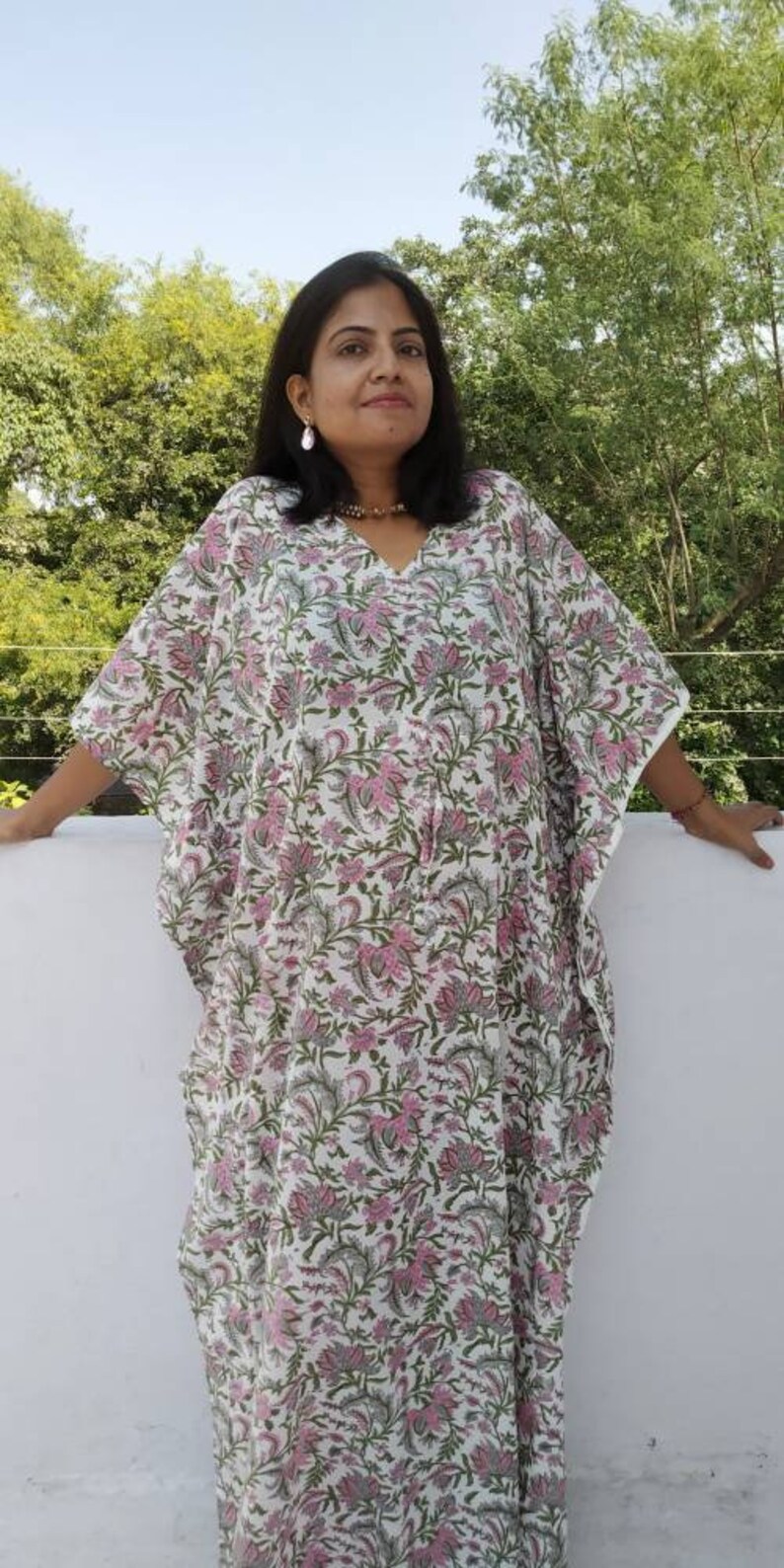 May include: A white kaftan with a pink and green floral print. The kaftan has a V-neck and long sleeves.