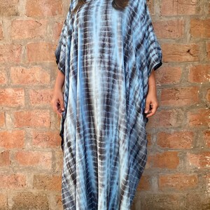 May include: A long, flowing blue and black tie-dye kaftan dress with a relaxed fit. The dress has a round neckline and short sleeves.