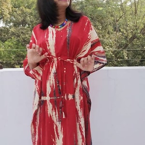 Puede incluir: Una kaft&aacute;n de color rojo y blanco con estampado tie-dye y una silueta larga y fluida. La kaft&aacute;n tiene cuello en V y un lazo en la cintura.