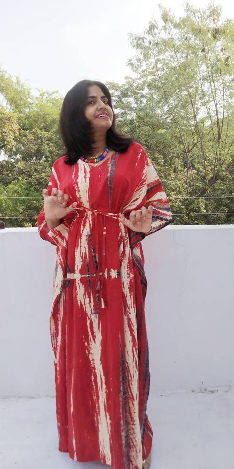 Puede incluir: Una kaft&aacute;n de color rojo y blanco con estampado tie-dye y una silueta larga y fluida. La kaft&aacute;n tiene cuello en V y un lazo en la cintura.