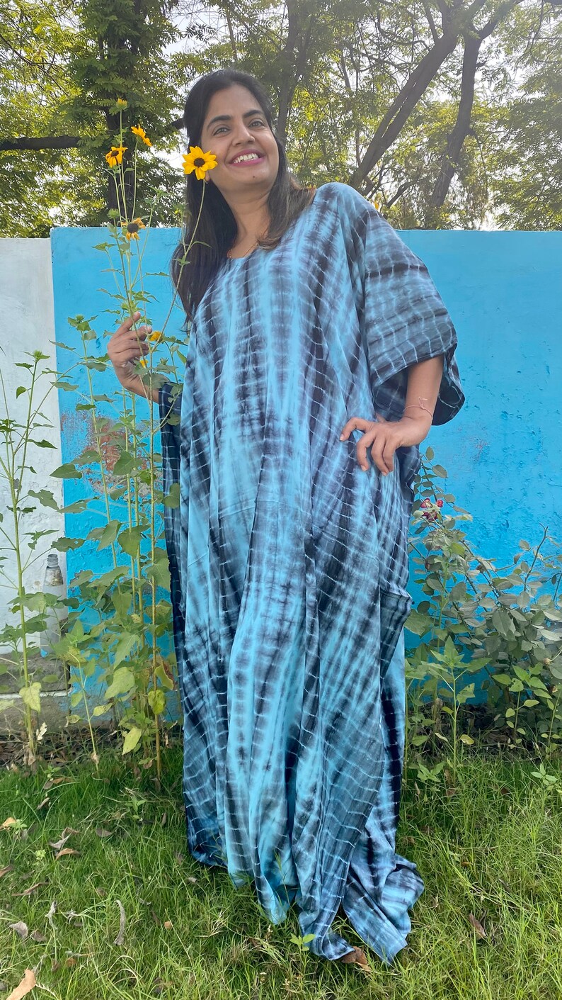 May include: A woman wearing a blue and black tie-dye kaftan dress. The dress has a loose, flowing fit and is made of a soft, comfortable fabric.
