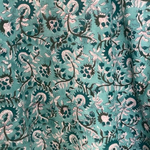 May include: Teal fabric with a white and dark green floral pattern. The fabric has a soft, flowing texture.