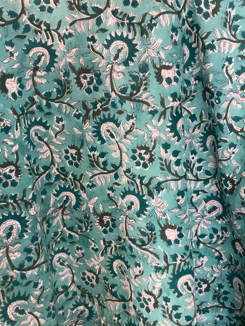 May include: Teal fabric with a white and dark green floral pattern. The fabric has a soft, flowing texture.