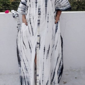 Op de afbeelding: Een witte maxi-jurk met een zwart tie-dye patroon. De jurk heeft een knoopsluiting aan de voorkant en zakken aan de zijkanten.
