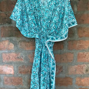 May include: A turquoise blue kaftan with a floral print. The kaftan has a V-neckline and short sleeves. It is made of a lightweight fabric and has a tie at the waist.