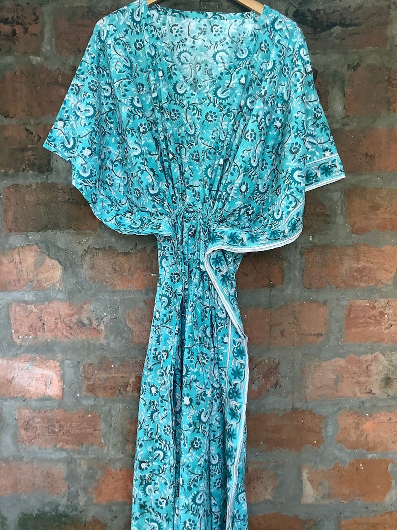 May include: A turquoise blue kaftan with a floral print. The kaftan has a V-neckline and short sleeves. It is made of a lightweight fabric and has a tie at the waist.
