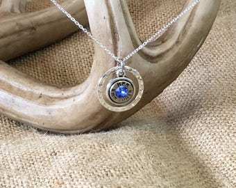 May include: A silver necklace with a hammered circle pendant featuring a blue gemstone and the text "9mm Ruger".