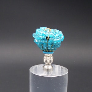 May include: A blue beaded lamp finial with a clear acrylic base. The finial is made of small, round beads that are strung together on wire. The base is a cylinder shape and is made of clear acrylic.
