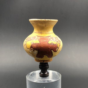 May include: A small ceramic vase with a brown bear design painted on it. The vase is yellow with brown and white accents. It is sitting on a clear acrylic stand.