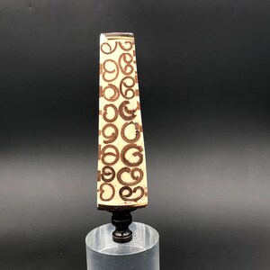 May include: A white ceramic lamp finial with a brown swirl pattern. The finial has a gold-colored metal base.