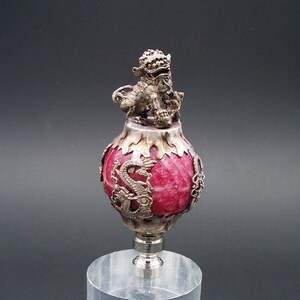 May include: A red and silver decorative lamp finial with a dragon and lion design. The finial is on a clear acrylic base.