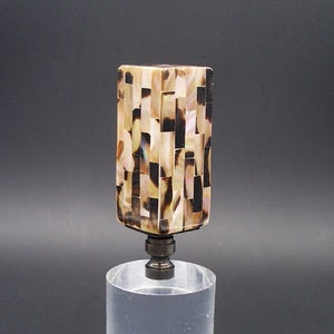 Peut inclure: Un embout de lampe en mosaïque de nacre irisée dans les tons brun, noir et blanc. L'embout est de forme carrée et repose sur une base en acrylique transparente.