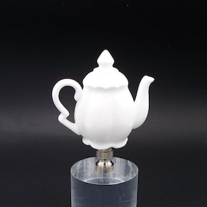 May include: White porcelain teapot lamp finial. The finial is a small, decorative piece that is used to top a lamp shade.