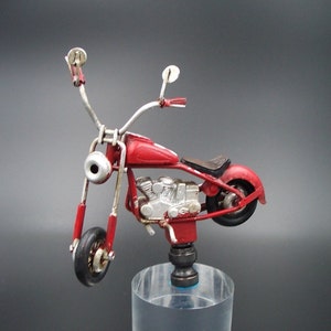 May include: A red metal toy motorcycle with a silver engine and chrome accents. The motorcycle is on a clear acrylic stand.