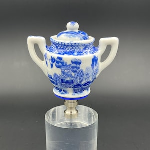 May include: A blue and white porcelain teapot finial with a lid and two handles. The teapot is decorated with a traditional Chinese pattern. The finial is mounted on a silver base.