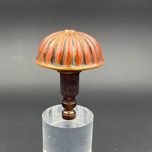 May include: A red and gold ceramic finial with a ribbed dome shape. The finial is mounted on a brass base.