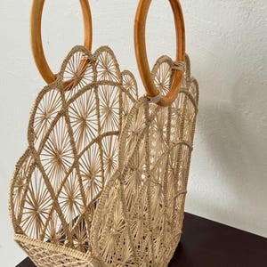 May include: A natural-coloured woven straw tote bag with a scalloped top edge and two wooden handles. The bag has a geometric pattern.