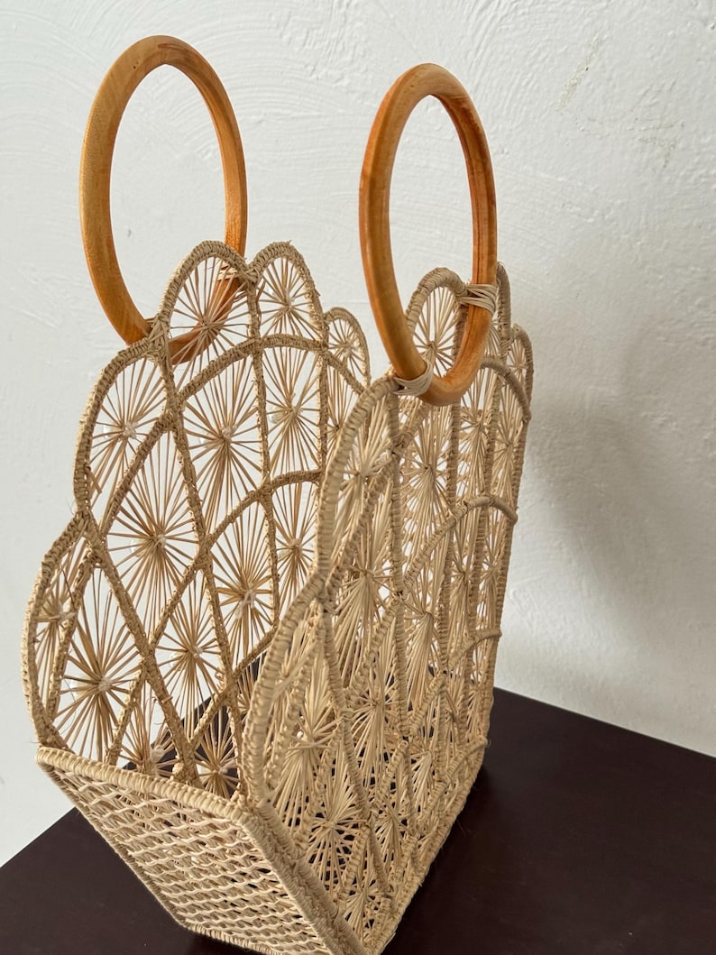 May include: A natural-coloured woven straw tote bag with a scalloped top edge and two wooden handles. The bag has a geometric pattern.