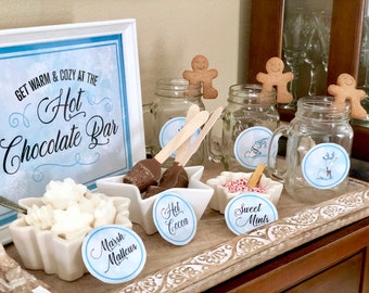 May include: A hot chocolate bar set up with a sign that reads "Get warm & cozy at the Hot Chocolate Bar". There are jars of hot chocolate, marshmallows, chocolate spoons, and candy canes.