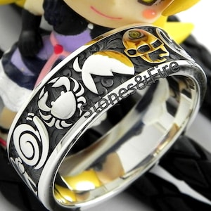 May include: A silver ring with a black and white design featuring a crab, a spiral, and a skull. The ring is engraved with the text "Stones & Fire".