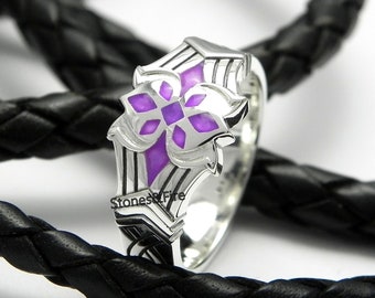 May include: A silver ring with a purple enamel design. The ring features a stylized flower with a geometric pattern. The ring is on a black braided leather background.