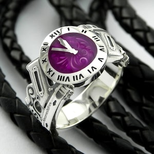 May include: A silver ring with a purple clock face and Roman numeral markings. The ring is engraved with the words "Stones & Fire".