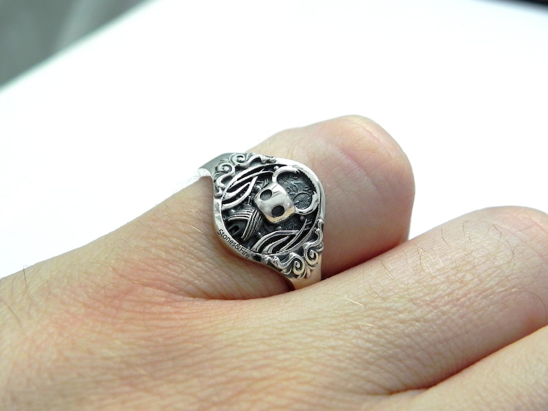 May include: A silver ring with a detailed design featuring a skull and wings.