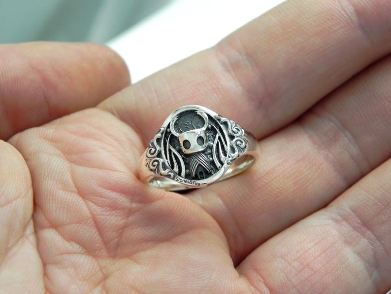 May include: A silver ring with a detailed design featuring a knight character with wings.