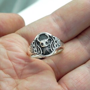May include: A silver ring with a detailed design featuring a knight character with wings.