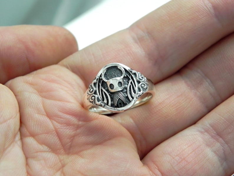 May include: A silver ring with a detailed design featuring a knight character with wings.