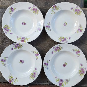 May include: Set of four white ceramic soup bowls with a floral design. The bowls have a scalloped edge and feature purple and green flowers.